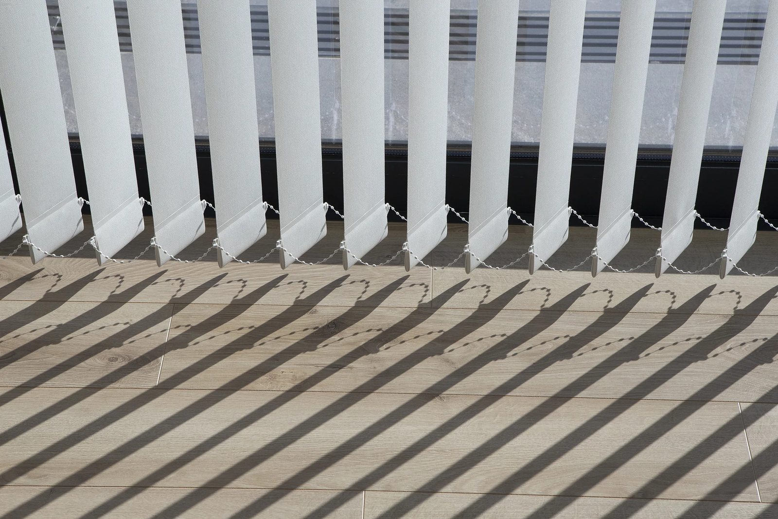 Detalle de lamas verticales blancas con sombras en tarima de madera